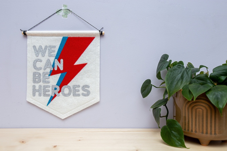 May include: White felt banner with a red and blue lightning bolt and the text "WE CAN BE HEROES" in silver glitter lettering.