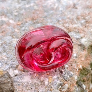 May include: A deep red glass bead with a swirling pattern inside. The bead is smooth and shiny.