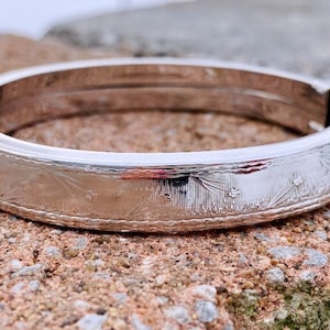 Peut inclure: Un bracelet jonc en argent avec un motif gravé. Le bracelet est ouvert et possède un fermoir à charnière.