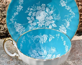 May include: A vintage teacup and saucer set with a blue and white floral pattern. The teacup has a white interior and a gold rim. The saucer has a scalloped edge.
