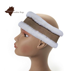 May include: A brown and white sheepskin ear warmer headband. The headband is made of soft, fluffy sheepskin and has a brown suede band.