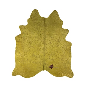 May include: A large, yellow cowhide rug with a speckled pattern. The rug is made of natural leather and has a rustic, bohemian style.