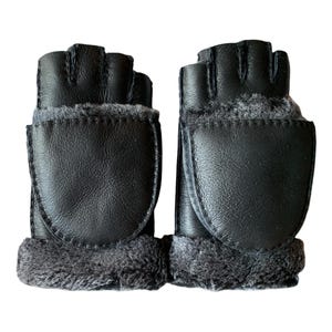 May include: A pair of black leather fingerless gloves with a flip-top mitten cover. The gloves have a soft, grey fur lining around the wrist area. The mitten covers are secured with a snap closure.
