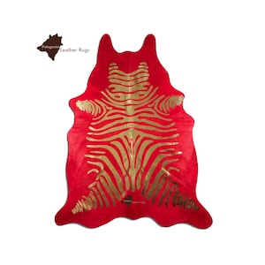 May include: Red cowhide rug with a gold zebra print. The rug is made of genuine leather and is a unique and stylish addition to any home.