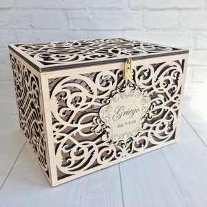 May include: A wooden box with a decorative, intricate cut-out design. The box has a lock and keyhole and a personalized tag that reads "Griego Est. 7-7-18".