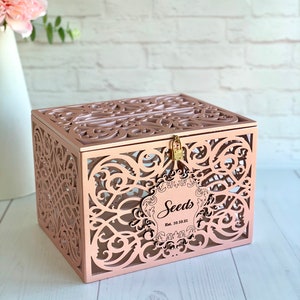 May include: Rose gold decorative box with a cutout design and a lock. The box has a label that says "Seeds Est. 10.10.21".