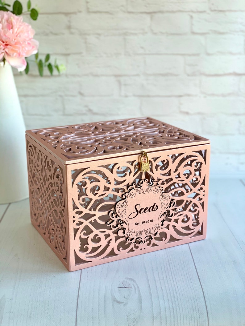 May include: Rose gold decorative box with a cutout design and a lock. The box has a label that says "Seeds Est. 10.10.21".