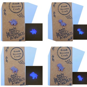 Op de afbeelding: Vier bruine kaarten met de tekst "Fresh Banana Craft" en "thanks for being a FRIEND-A-SAURUS" erop. Elke kaart heeft een klein paars dinosaurusbeeldje erop. De dinosaurusbeeldjes gloeien blauw in het donker.