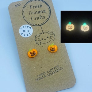 May include: A pair of orange glow-in-the-dark pumpkin earrings. The earrings are on a brown card with the text "BOO", "Fresh Banana Crafts", "Glow in the Dark", and "Fangs a lot for being a great fiend".