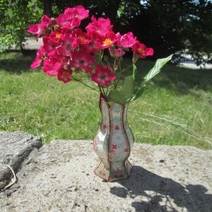 May include: A bouquet of pink roses in a white and red patterned vase. The vase is made of fabric and has a unique, stitched design.