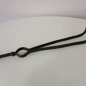 Op de afbeelding: Zwarte metalen haardtang met een ringvormige handgreep. De tang is ontworpen om houtblokken of andere voorwerpen uit een open haard te pakken en te tillen.
