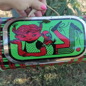 May include: Vintage metal lunchbox with a whimsical illustration of a girl and a monkey. The lunchbox has a red, green, and black plaid pattern on the sides. The main image features a girl with red hair and a monkey on a green background.
