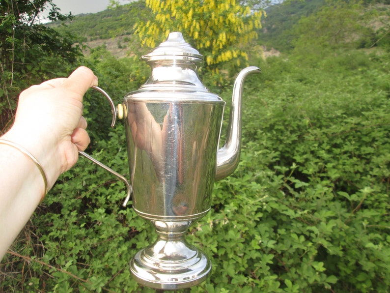 May include: A silver teapot with a rounded body and a curved spout. The teapot has a polished finish and a decorative handle.