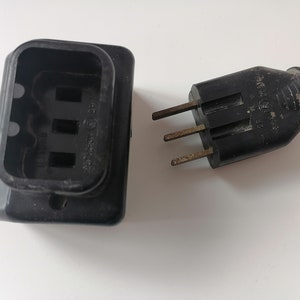 Puede incluir: Una toma de corriente negra y un enchufe negro de tres clavijas. El enchufe tiene una clavija de tierra.