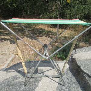 K&ouml;nnte beinhalten: Ein klappbarer Campingstuhl mit einer gr&uuml;n-wei&szlig;-rot gestreiften Stoffbespannung. Der Stuhl ist aus Metall und hat ein schlichtes Design.