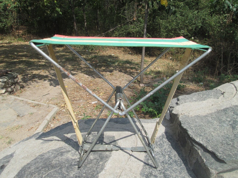K&ouml;nnte beinhalten: Ein klappbarer Campingstuhl mit einer gr&uuml;n-wei&szlig;-rot gestreiften Stoffbespannung. Der Stuhl ist aus Metall und hat ein schlichtes Design.