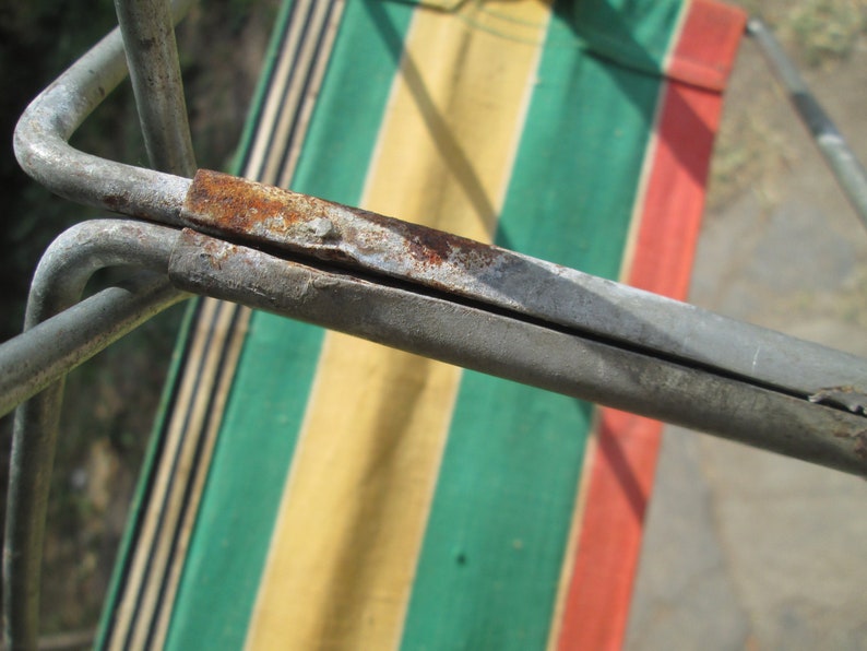 K&ouml;nnte beinhalten: Nahaufnahme eines Metallrahmens mit sichtbarem Rost, der an einem gestreiften Stoff mit gr&uuml;nen, gelben und roten Streifen befestigt ist.