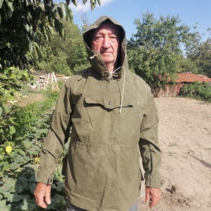 Könnte beinhalten: Eine olivgrüne Anorak-Jacke mit Kapuze, einer großen Fronttasche mit Druckknopfverschluss, langen Ärmeln mit geknöpften Manschetten und einer Kordel am Hals. Die Jacke verfügt über eine Taillierung und eine Kapuze, die den Kopf bedeckt.