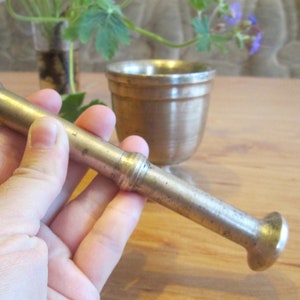 May include: A silver mortar and pestle set. The pestle is held in a hand and the mortar is in the background.