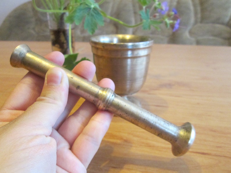 May include: A silver mortar and pestle set. The pestle is held in a hand and the mortar is in the background.