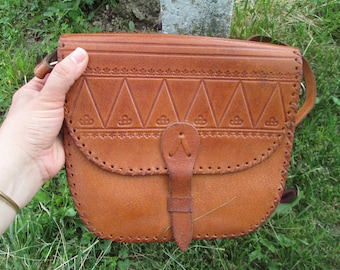May include: A brown leather shoulder bag with a flap closure and a decorative embossed design. The bag has a strap and a small pocket on the front.