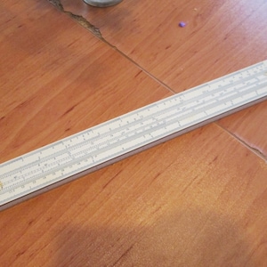 Może przedstawiać: Biała suwmiarka z czarnymi oznaczeniami. Suwmiarka to narzędzie używane do obliczeń matematycznych.