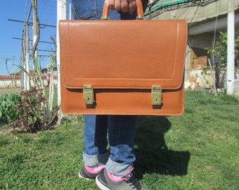 May include: A brown leather briefcase with brass clasps and a textured surface.