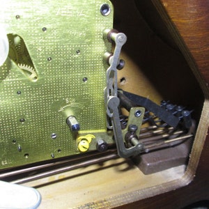 May include: Close-up of a clock mechanism with a brass plate, gears, and a metal lever. The clock face is visible in the background.