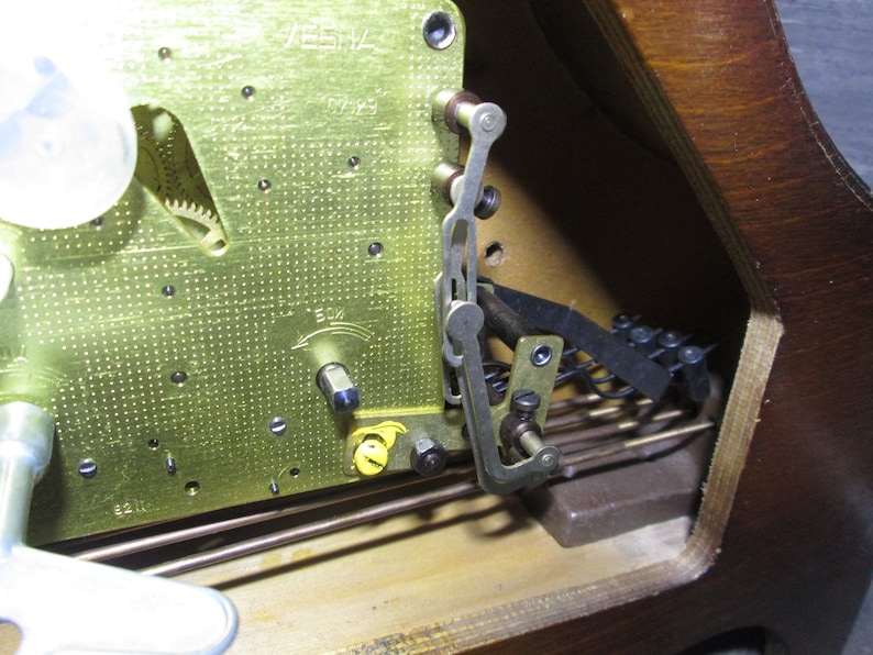 May include: Close-up of a clock mechanism with a brass plate, gears, and a metal lever. The clock face is visible in the background.