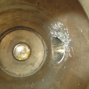 May include: Close-up view of the inside of a metal cylinder. The cylinder has a circular opening with a smaller, round opening inside. There is a small, rectangular opening on the right side of the cylinder.