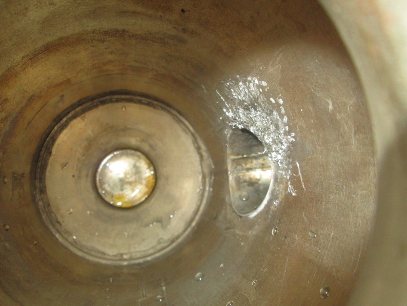 May include: Close-up view of the inside of a metal cylinder. The cylinder has a circular opening with a smaller, round opening inside. There is a small, rectangular opening on the right side of the cylinder.