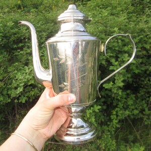 May include: A silver teapot with an ornate design and a handle. The teapot has a lid and a spout. The teapot is sitting on a table.