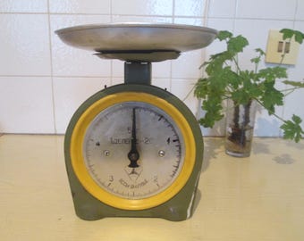 May include: A vintage green and yellow kitchen scale with a silver weighing pan. The scale has a round dial with black markings and the words "ВЕСЪ БЫТОВОЙ" in Cyrillic script.