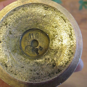 May include: Close-up of the bottom of a brass candlestick with the number "1120" stamped on the base.
