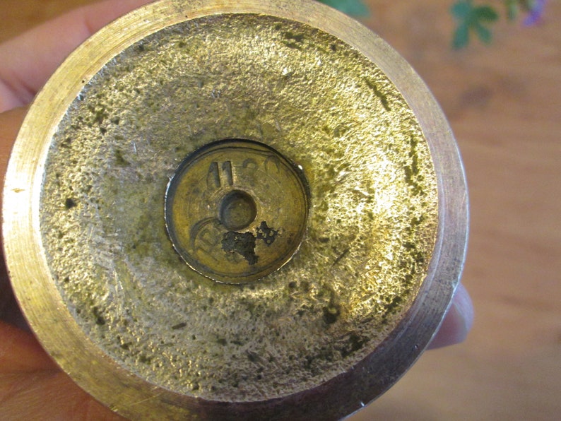 May include: Close-up of the bottom of a brass candlestick with the number "1120" stamped on the base.