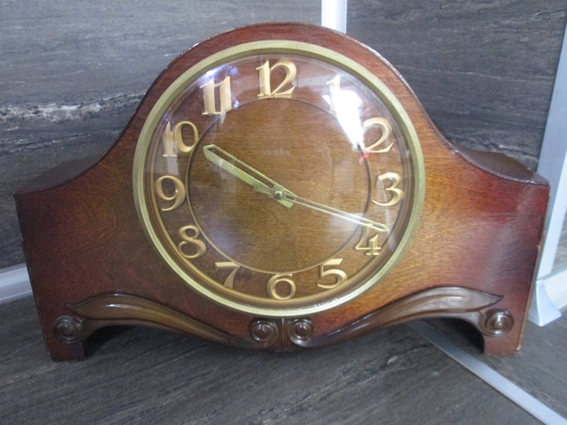 May include: A vintage wooden mantel clock with a gold-toned face and black hands. The clock has a curved, ornate base and a glass cover over the face.
