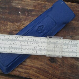Może przedstawiać: Biała suwmiarka z niebieskim skórzanym etui. Suwmiarka ma przezroczysty plastikowy suwak i jest oznaczona liczbami i skalami. Etui ma logo w kształcie rombu.