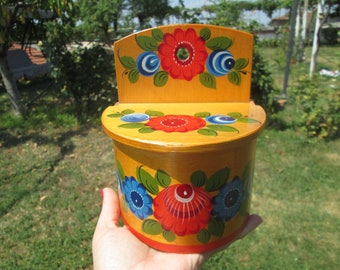 May include: A yellow wooden salt or pepper shaker with a hinged lid. The shaker is decorated with hand-painted flowers in red, blue, and green.