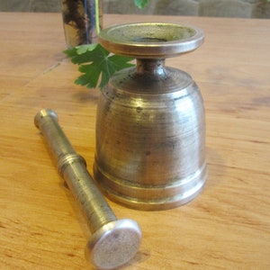 May include: A silver mortar and pestle set. The mortar is a bell-shaped bowl with a wide base and a narrow opening. The pestle is a long, cylindrical rod with a rounded end.