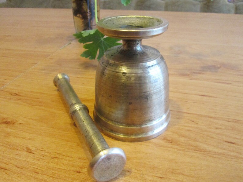 May include: A silver mortar and pestle set. The mortar is a bell-shaped bowl with a wide base and a narrow opening. The pestle is a long, cylindrical rod with a rounded end.