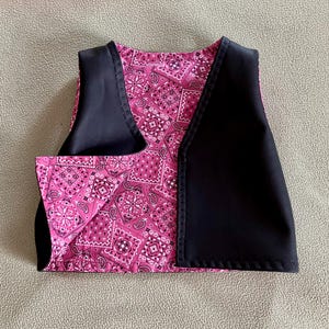 Puede incluir: Un chaleco peque&ntilde;o con un estampado de cachemira rosa y detalles en negro. El chaleco tiene un dise&ntilde;o cl&aacute;sico con cuello en V y probablemente sea para un ni&ntilde;o o una mascota peque&ntilde;a. La tela rosa est&aacute; cubierta con un dise&ntilde;o de cachemira blanco y negro.