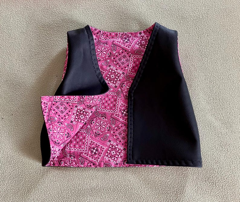 Puede incluir: Un chaleco peque&ntilde;o con un estampado de cachemira rosa y detalles en negro. El chaleco tiene un dise&ntilde;o cl&aacute;sico con cuello en V y probablemente sea para un ni&ntilde;o o una mascota peque&ntilde;a. La tela rosa est&aacute; cubierta con un dise&ntilde;o de cachemira blanco y negro.