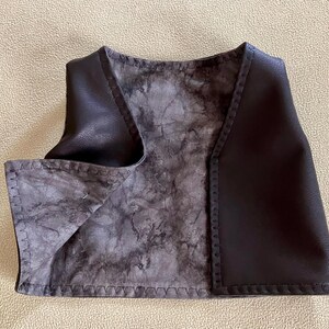 Puede incluir: Un chaleco de cuero marr&oacute;n oscuro con un forro interior gris y negro veteado. El chaleco tiene cuello en V y est&aacute; cosido a lo largo de los bordes. El chaleco es de talla peque&ntilde;a.