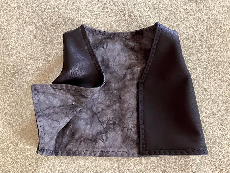 Puede incluir: Un chaleco de cuero marr&oacute;n oscuro con un forro interior gris y negro veteado. El chaleco tiene cuello en V y est&aacute; cosido a lo largo de los bordes. El chaleco es de talla peque&ntilde;a.