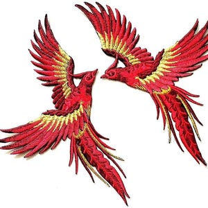 May include: Two embroidered patches featuring a phoenix design. The birds are depicted in flight with outstretched wings. The patches are primarily red with yellow and gold accents, showcasing detailed stitching.