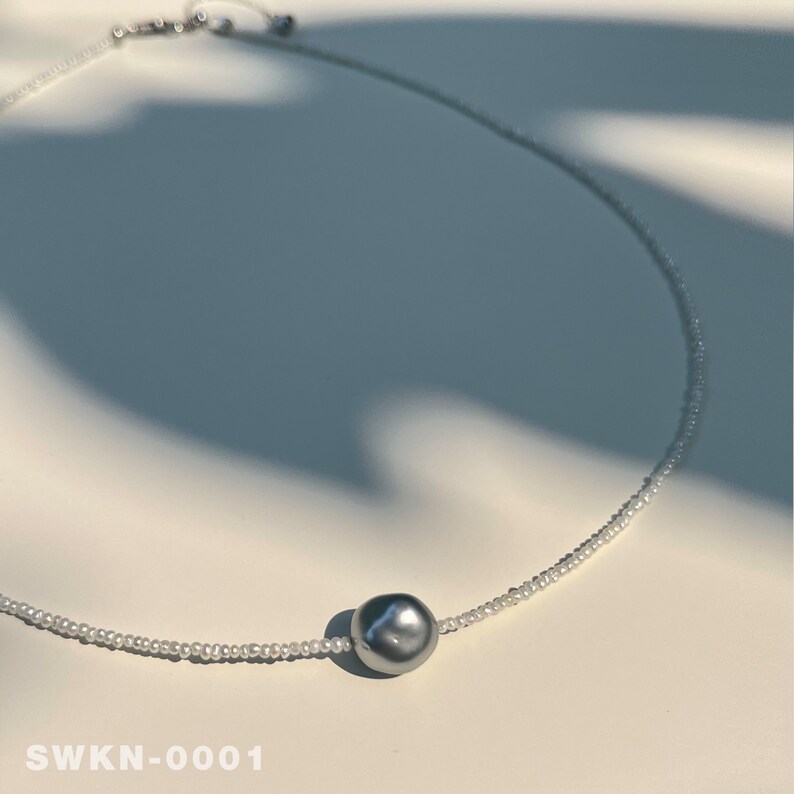 May include: A delicate silver necklace with a single large grey pearl pendant. The necklace is made of tiny white beads.