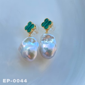 May include: A pair of gold earrings with green clover charms and large white baroque pearls. The earrings are on a white surface with the text "EP-0044".