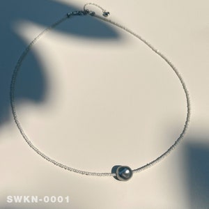 May include: A delicate silver chain necklace with a single large gray pearl pendant. The necklace is made of tiny white beads.