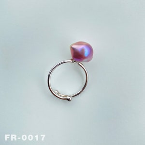 May include: A silver ring with a large, iridescent pink pearl. The ring is open and adjustable.