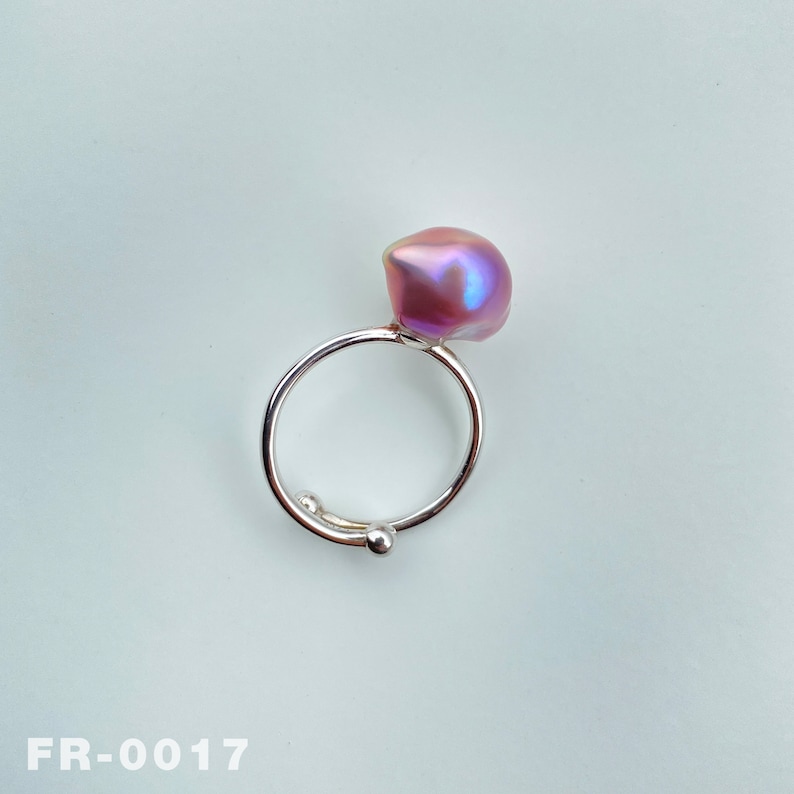 May include: A silver ring with a large, iridescent pink pearl. The ring is open and adjustable.
